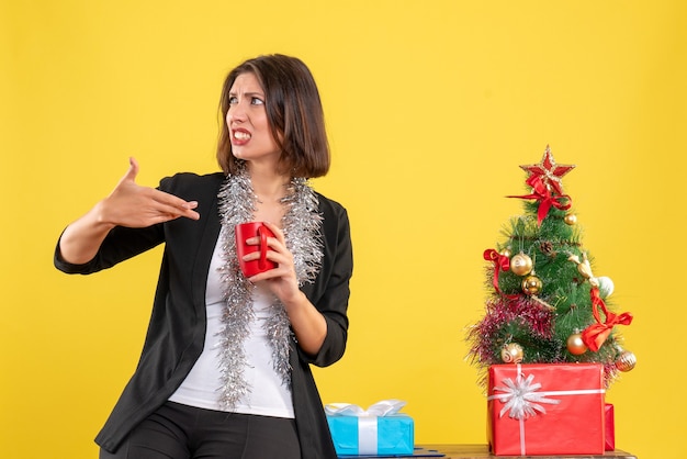 Ambiance De Noël Avec Une Belle Dame émotionnelle Debout Dans Le Bureau Et Tenant Une Tasse Rouge Au Bureau Sur Jaune