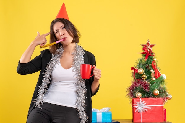 Ambiance de Noël avec drôle belle dame tenant la tasse rouge au bureau sur jaune