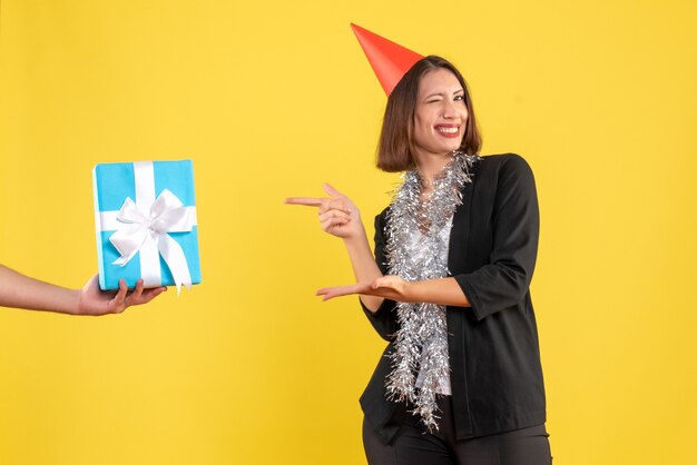 Ambiance de Noël avec une femme d'affaires heureuse et excitée en costume avec un chapeau de Noël pointant la main tenant un cadeau sur le jaune