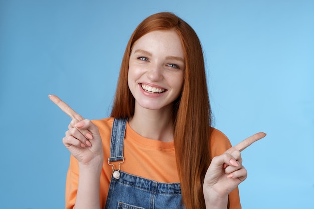 Amical heureux riant jolie fille rousse étudiante montrant beaucoup d'opportunités conseils faire un choix pointant sur le côté gauche droite introduisant un produit différent souriant joyeusement, fond bleu.