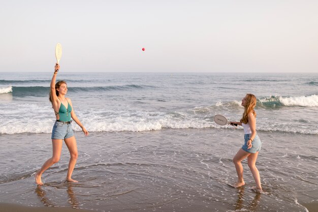 Amies appréciant jouer avec tennis au bord de la mer