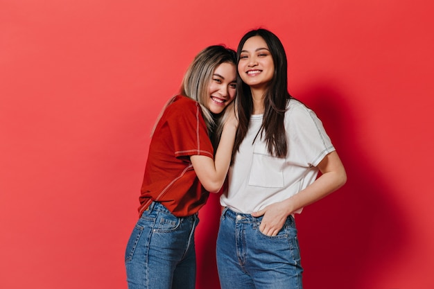 Les amies asiatiques souriantes posent sur le mur rouge