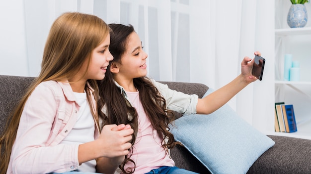 Amies assis sur le canapé prenant selfie sur téléphone intelligent