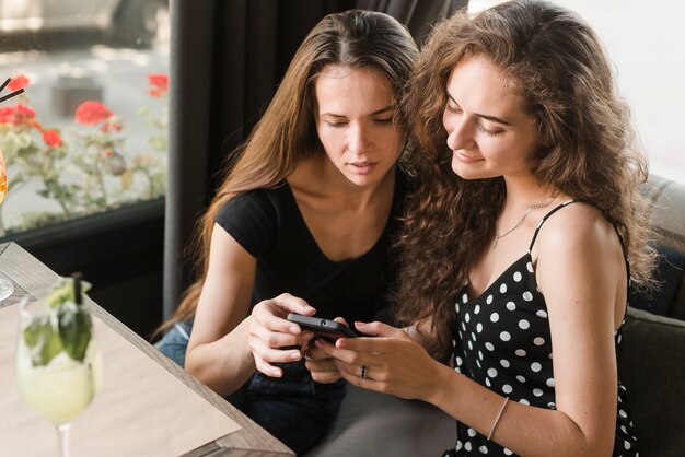 Amies assis dans un restaurant en regardant téléphone intelligent