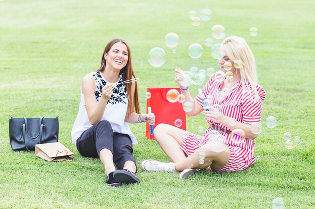 Amies assises sur l&#39;herbe verte soufflant des bulles avec la baguette