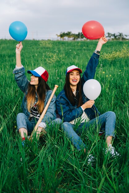 Amies avec des ballons dans des casquettes colorées rire dans le parc