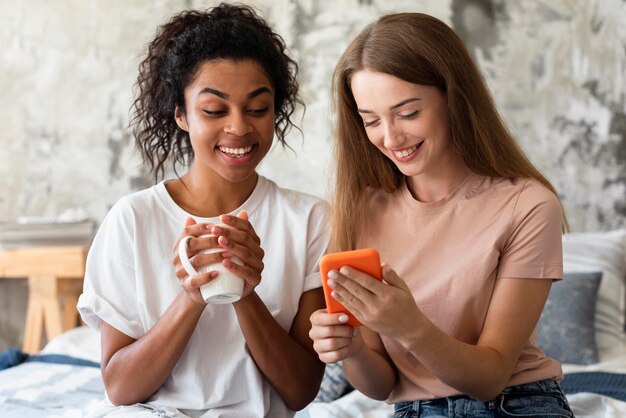 Amies à la maison avec smartphone et tasse