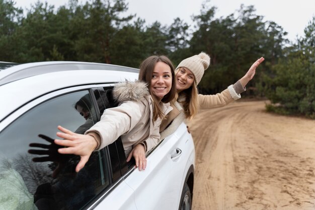 Des amies sortent de la voiture de la fenêtre en voyageant