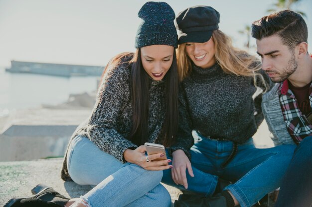 Amis assis au bord de l&#39;eau avec un smartphone