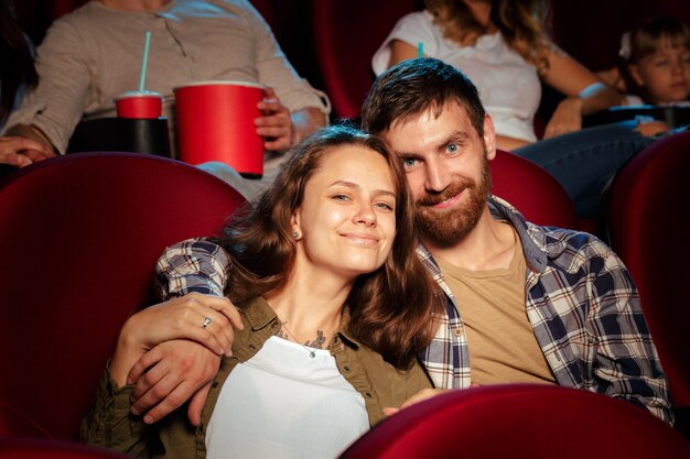 Des amis assis au cinéma regardent un film en train de manger du pop-corn et de boire de l'eau.