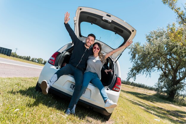 Amis assis sur le coffre d&#39;une voiture faisant signe de paix