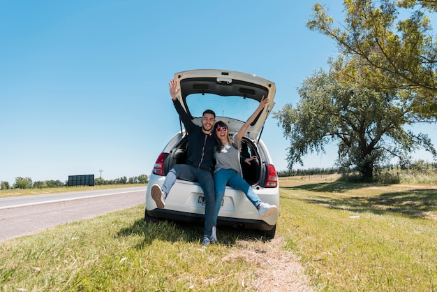 Amis assis sur le coffre d&#39;une voiture faisant signe de paix