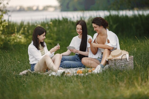 Amis assis sur l'herbe. Les filles sur une couverture. Femme en chemise blanche.