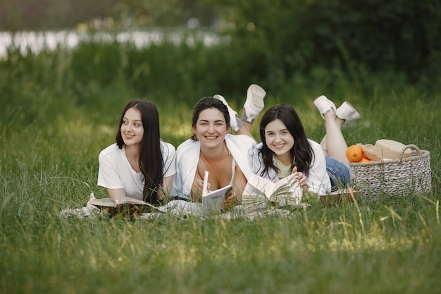 Amis assis sur l'herbe. Les filles sur une couverture. Femme en chemise blanche.