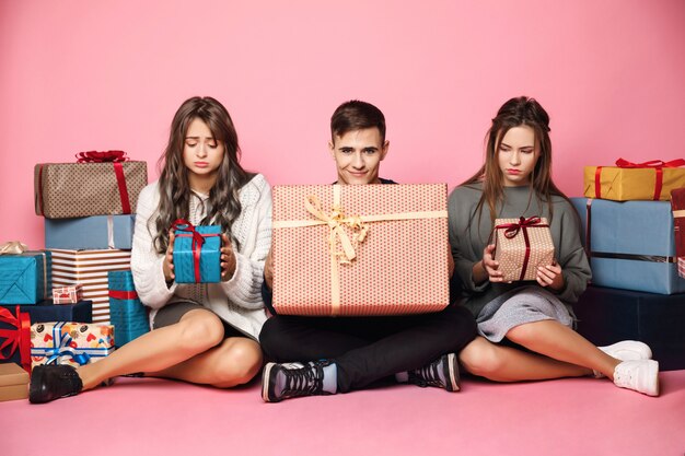 Amis assis parmi les cadeaux de Noël. Guy tenant une grande boîte, peu de femme.