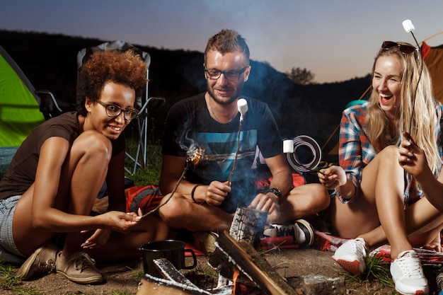 Amis assis près de feu de joie, souriant, jouant de la guitare Camping grill guimauve.