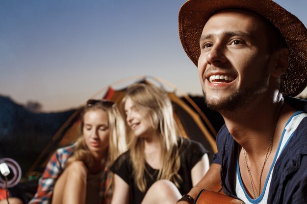 Amis Assis Près De Feu De Joie, Souriant, Jouant De La Guitare Camping Grill Guimauve.