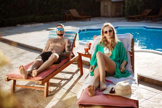 Amis bronzer, allongé sur des chaises près de la piscine