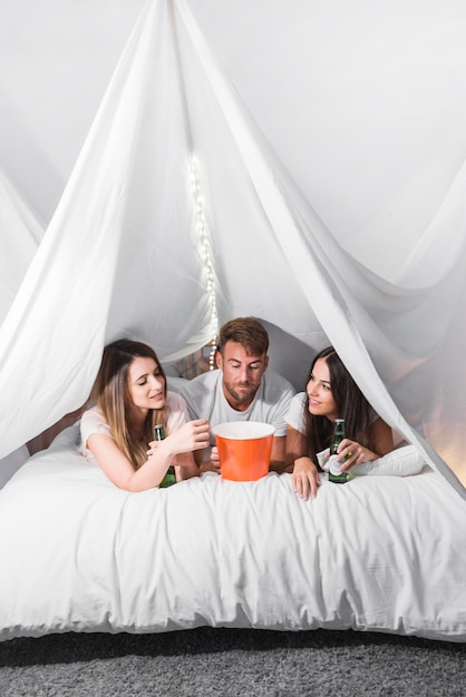 Photo gratuite amis, couché sur un lit douillet en profitant des boissons et du pop-corn dans la chambre