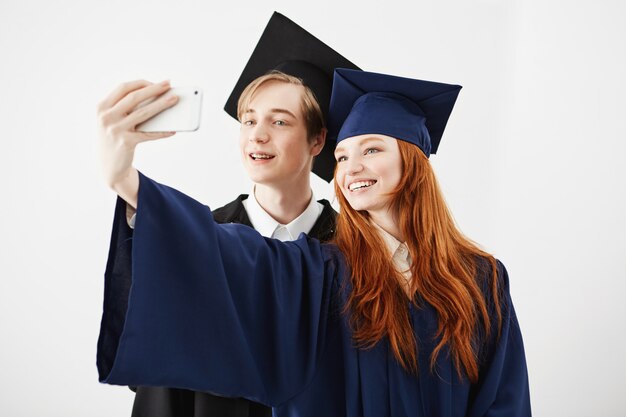 Amis diplômés de l'université en majuscules souriant faisant selfie.