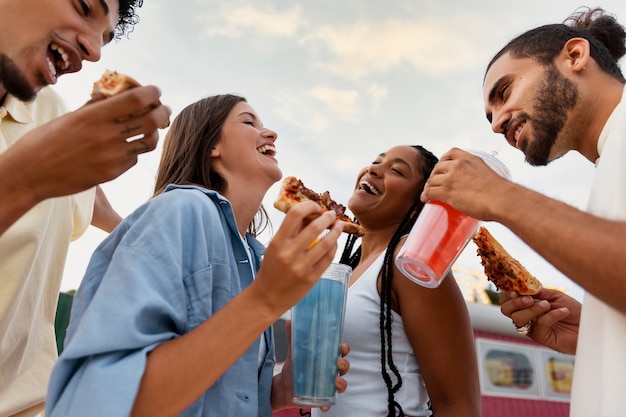 Amis heureux à faible angle avec pizza et boissons