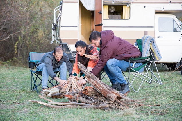 Amis hipster faisant ensemble un feu de camp dans la forêt de montagne. Amis campant avec un camping-car rétro.
