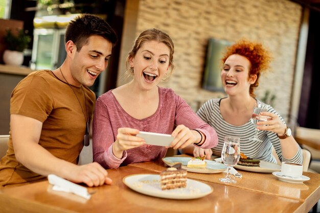 Amis joyeux s'amusant tout en prenant une photo de leur dessert dans un café