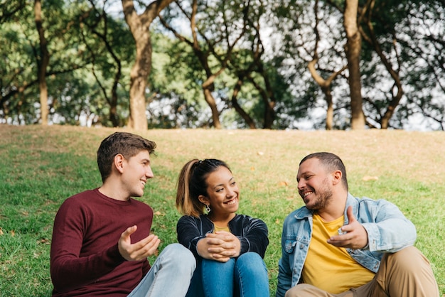 Amis multiethniques parler et assis sur l&#39;herbe dans le parc