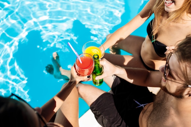Amis parlant, souriant, buvant des cocktails, se reposant, se relaxant près de la piscine