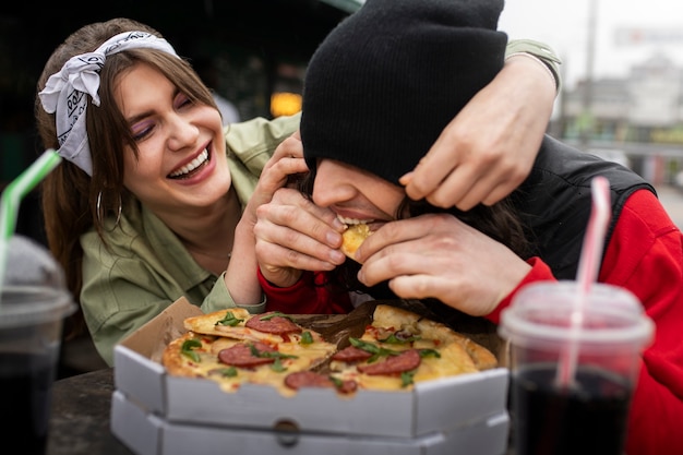 Amis de plan moyen mangeant de la restauration rapide d'une manière amusante