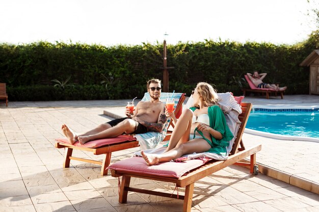 Amis souriant, buvant des cocktails, allongé sur des chaises près de la piscine