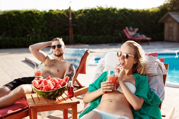 Amis souriant, buvant des cocktails, allongé sur des chaises près de la piscine