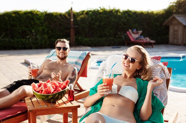 Amis souriant, buvant des cocktails, allongé sur des chaises près de la piscine