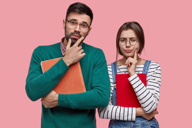 Photo gratuite les amis de l'université ont des expressions réfléchies, portent un vieux livre et un bloc-notes, réfléchissent à la bonne décision