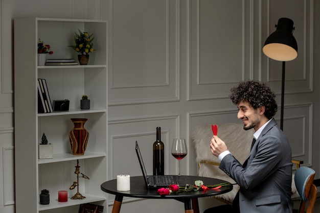 Photo gratuite amour virtuel beau mec mignon en costume avec du vin sur une date d'ordinateur à distance tenant un coeur en papier