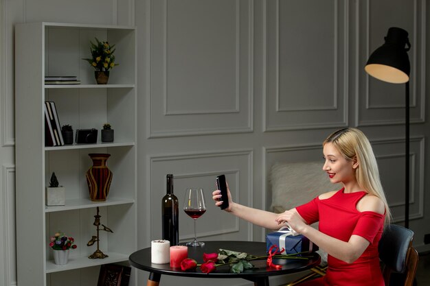 Amour virtuel jolie fille en robe rouge à distance date avec vin tenant cadeau et téléphone