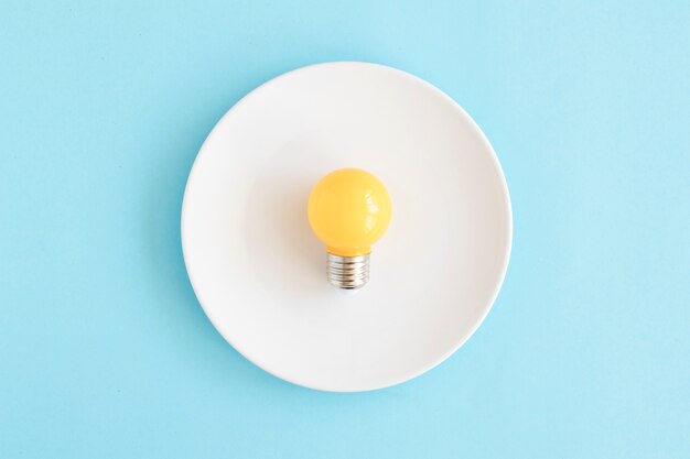 Ampoule jaune-clair sur un plat blanc sur la toile de fond bleue