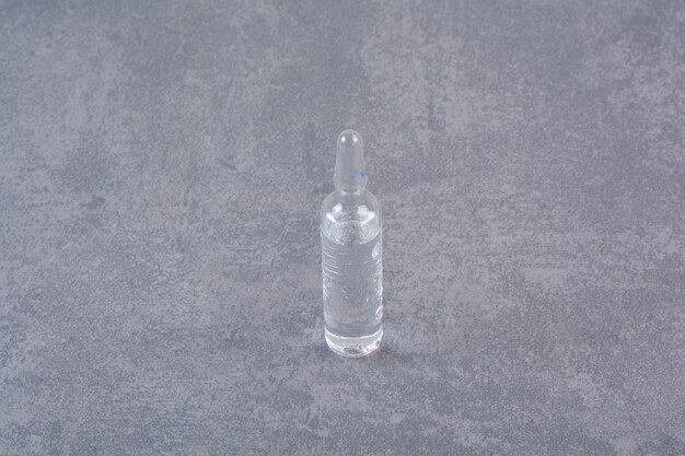 Ampoule médicale transparente sur table en marbre.