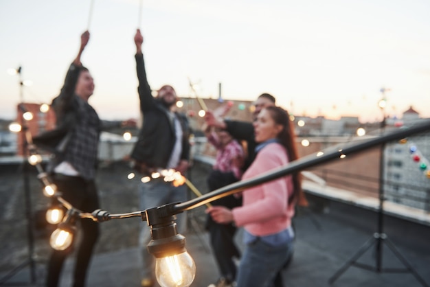 Les ampoules sont allumées. Photo mise au point. Jouer avec des cierges magiques sur le toit. Groupe de jeunes beaux amis