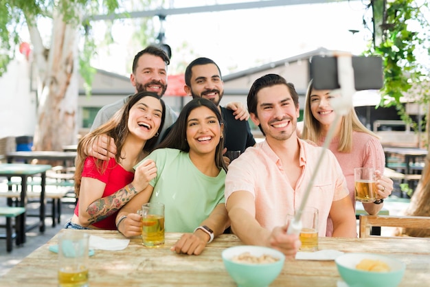 Amusant groupe multiracial d'amis souriant pour un selfie tout en étant assis ensemble au bar. Amis proches du collège prenant une photo avec un smartphone pour publier sur les réseaux sociaux