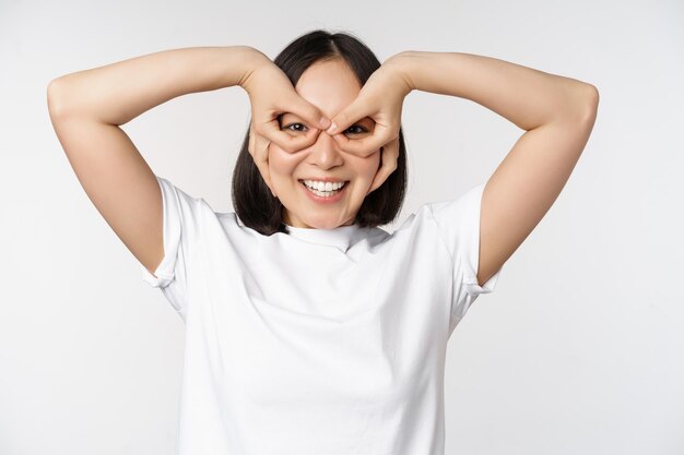 Amusante jeune femme asiatique fille coréenne faisant des yeux lunettes geste regardant heureux à la caméra debout sur fond blanc