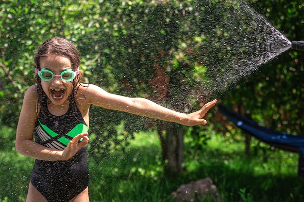 Photo gratuite amusante petite fille jouant avec un tuyau d'arrosage dans une cour ensoleillée