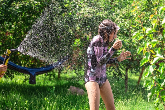 Photo gratuite amusante petite fille jouant avec un tuyau d'arrosage dans une cour ensoleillée