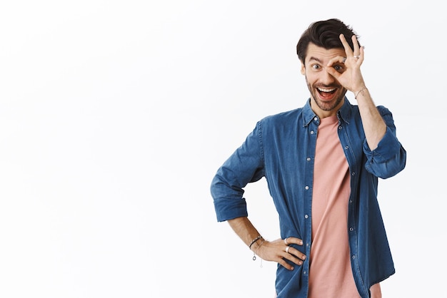 Photo gratuite amusé fasciné beau mec barbu avec des cheveux en désordre montrant bien ou un geste de confirmation faire un cercle sur les yeux et souriant impressionné se sentir heureux taux bon choix fond blanc