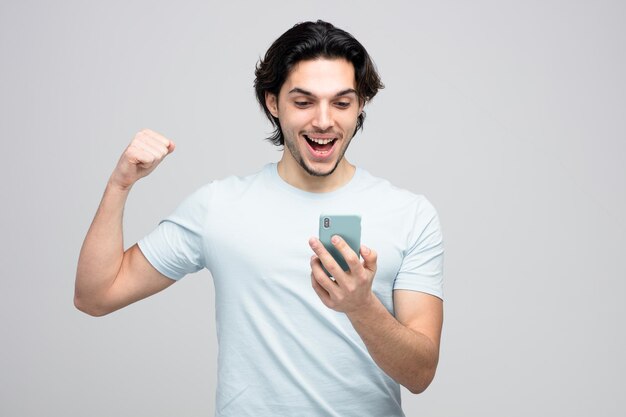 amusé jeune bel homme tenant et regardant un téléphone portable montrant un geste fort isolé sur fond blanc