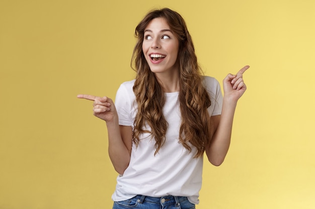 Amusée joyeuse souriante heureuse jeune femme aux cheveux bouclés, les cheveux châtains observent curieusement l'espace de copie souriant admiration joie pointant sur le côté faisant le choix impressionné satisfait tourner à gauche.