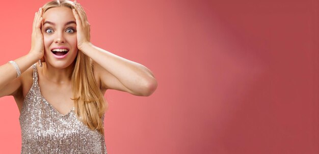 Amusée, surprise, excitée, jeune femme blonde et attrayante dans une robe argentée étincelante et élégante tient la tête.