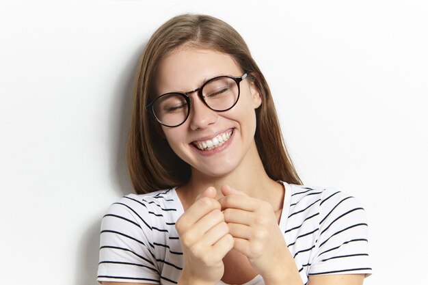 Amusement, joie, émotions humaines positives et concept de sentiments. Belle jeune femme joyeuse à lunettes et chemise de marin fermant les yeux et riant aux éclats, montrant ses dents blanches droites