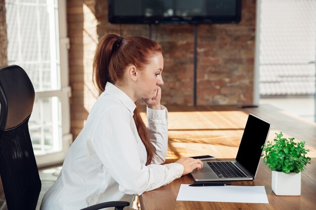 Analisant. Jeune femme caucasienne en tenue d'affaires travaillant au bureau