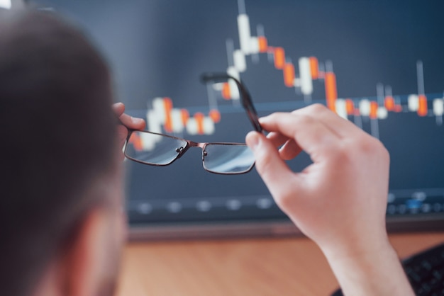 Analyse des données. Gros plan d'un jeune homme d'affaires qui tient des lunettes et regarde la gff tout en travaillant dans un bureau de création